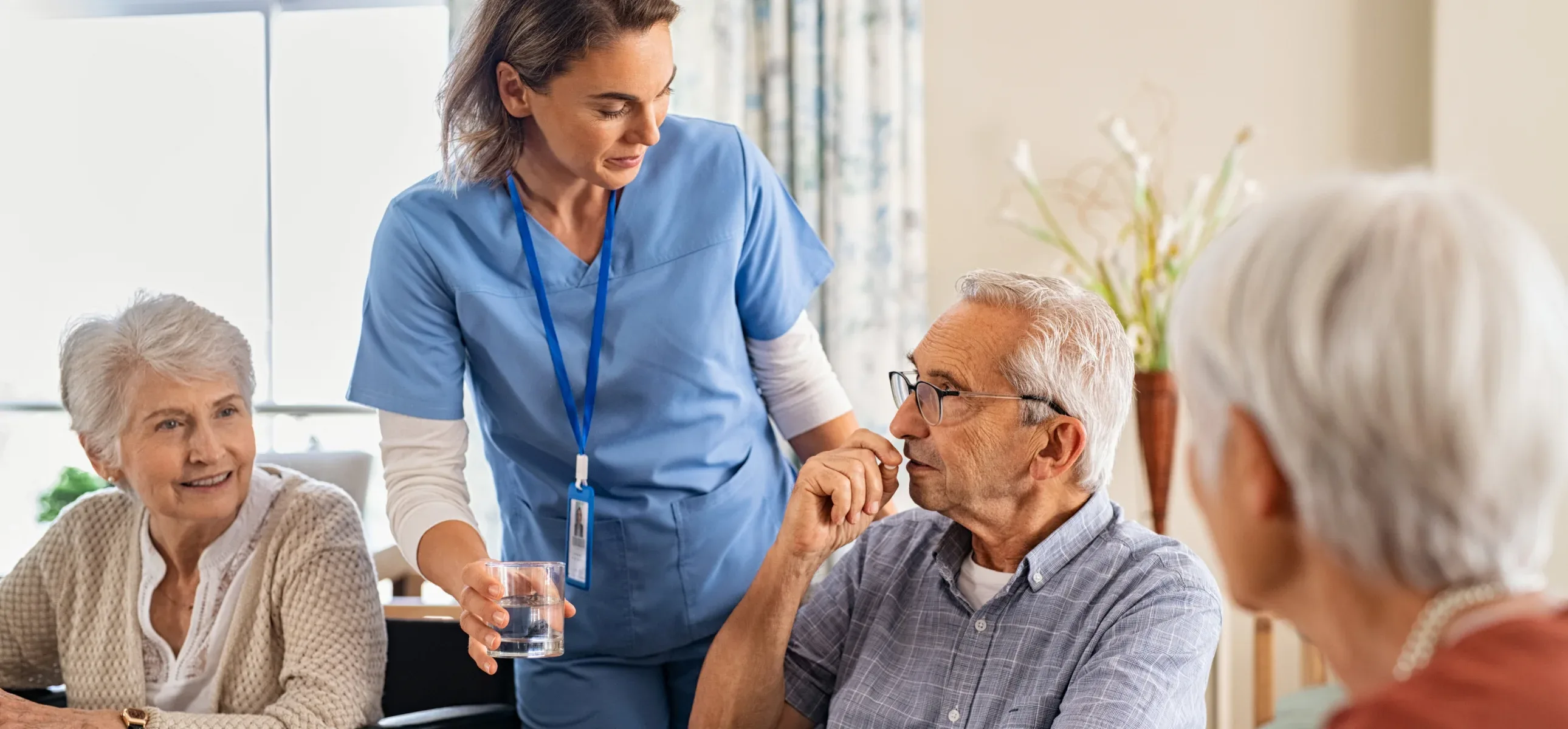 A nurse assists an elderly person at a table, providing care and support in a warm, compassionate environment.