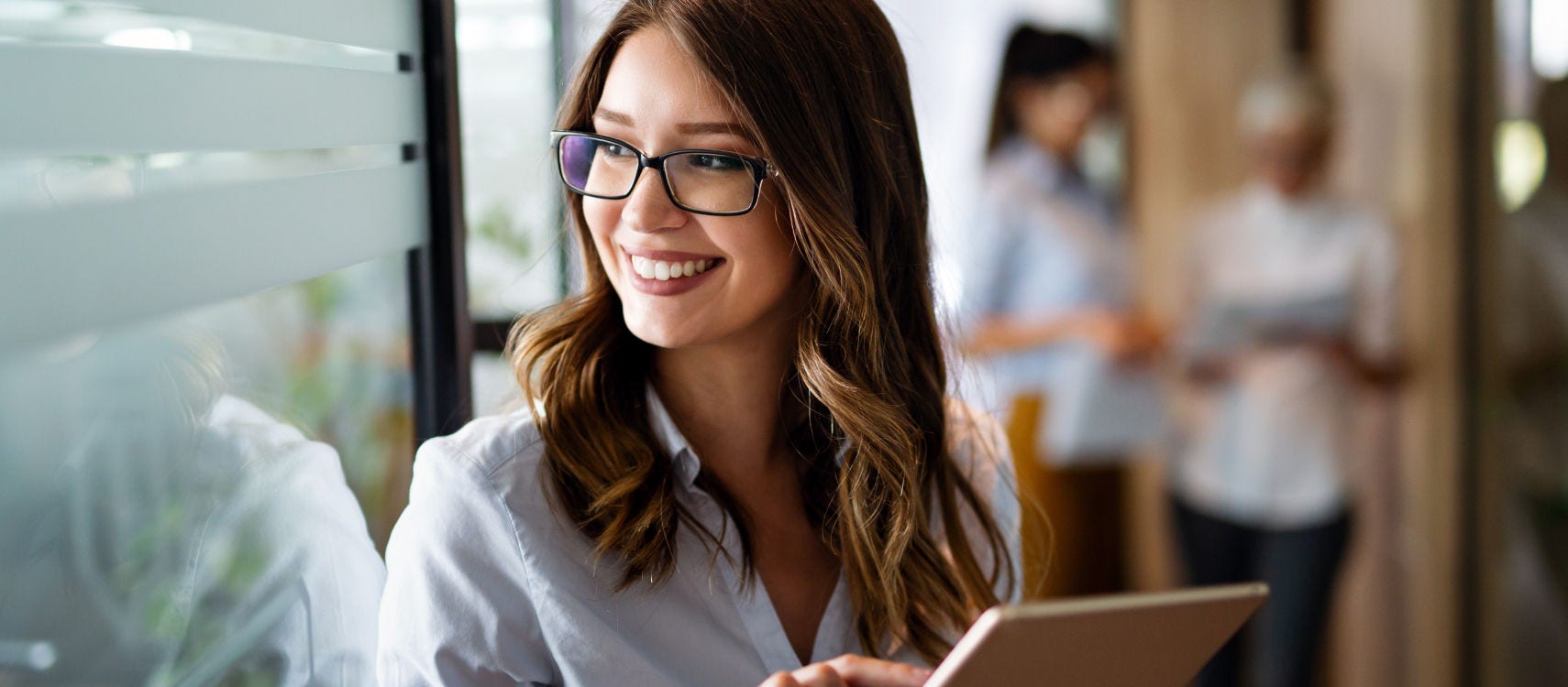 A woman wearing glasses is focused on a tablet computer she is holding in her hands.