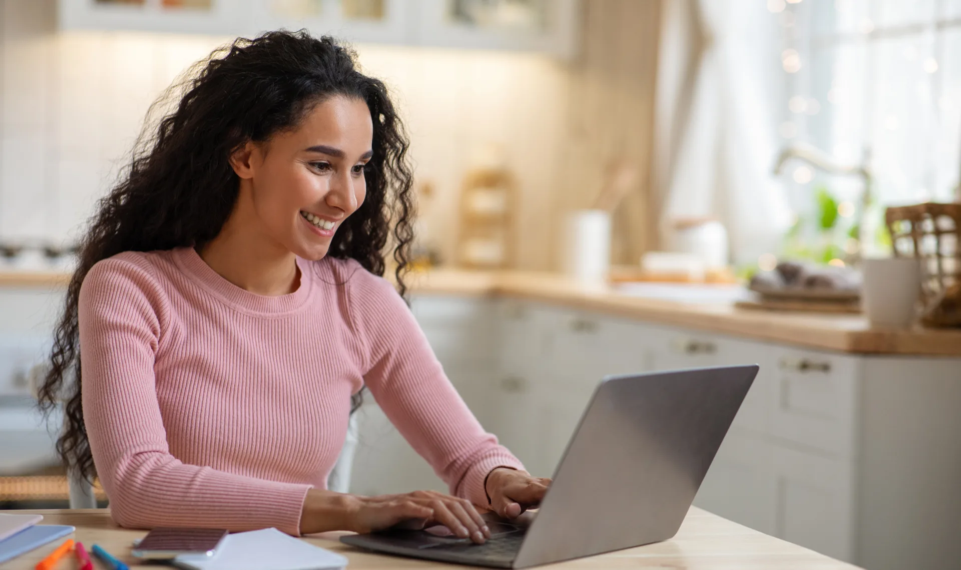 A woman smiles brightly while working on her laptop, showcasing a moment of joy and productivity.