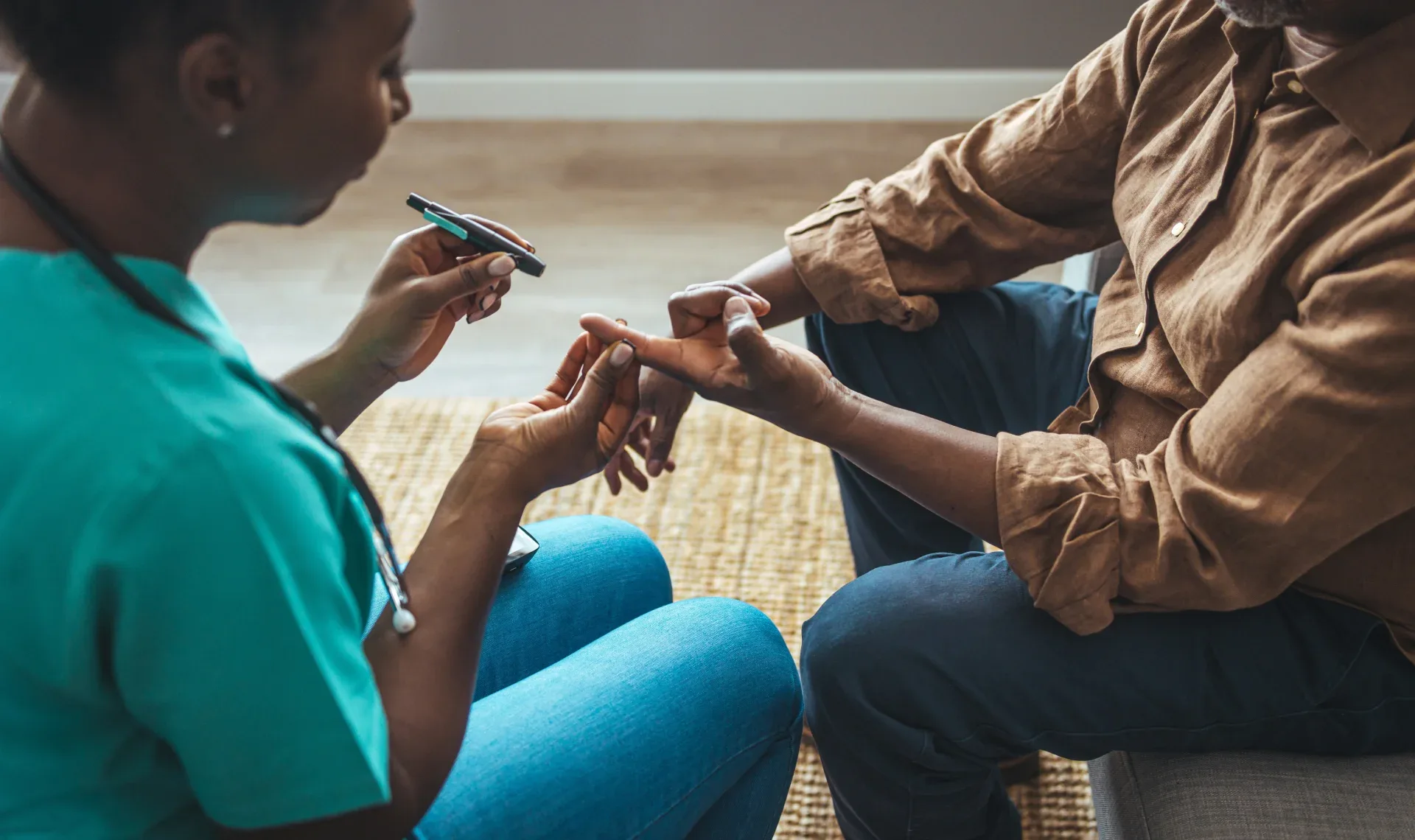 A person in scrubs holds the finger of another person, preparing to do a finger stick.