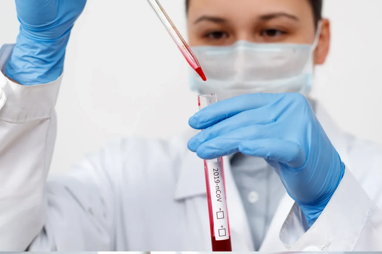 A woman in a lab coat holds a blood tube, showcasing her role in a scientific or medical environment.