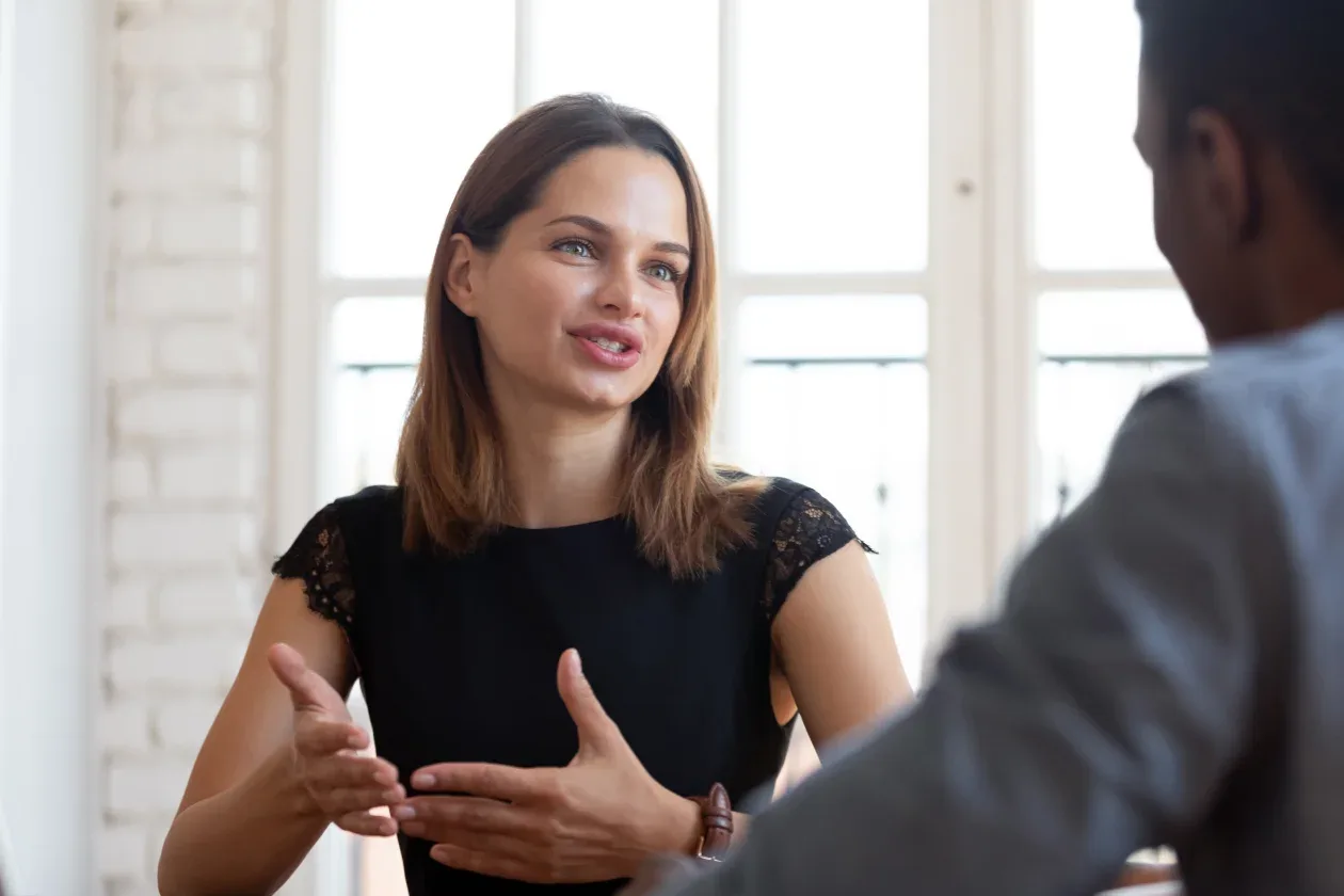 A woman engages in conversation with a man in a professional office setting, both appearing focused and attentive.