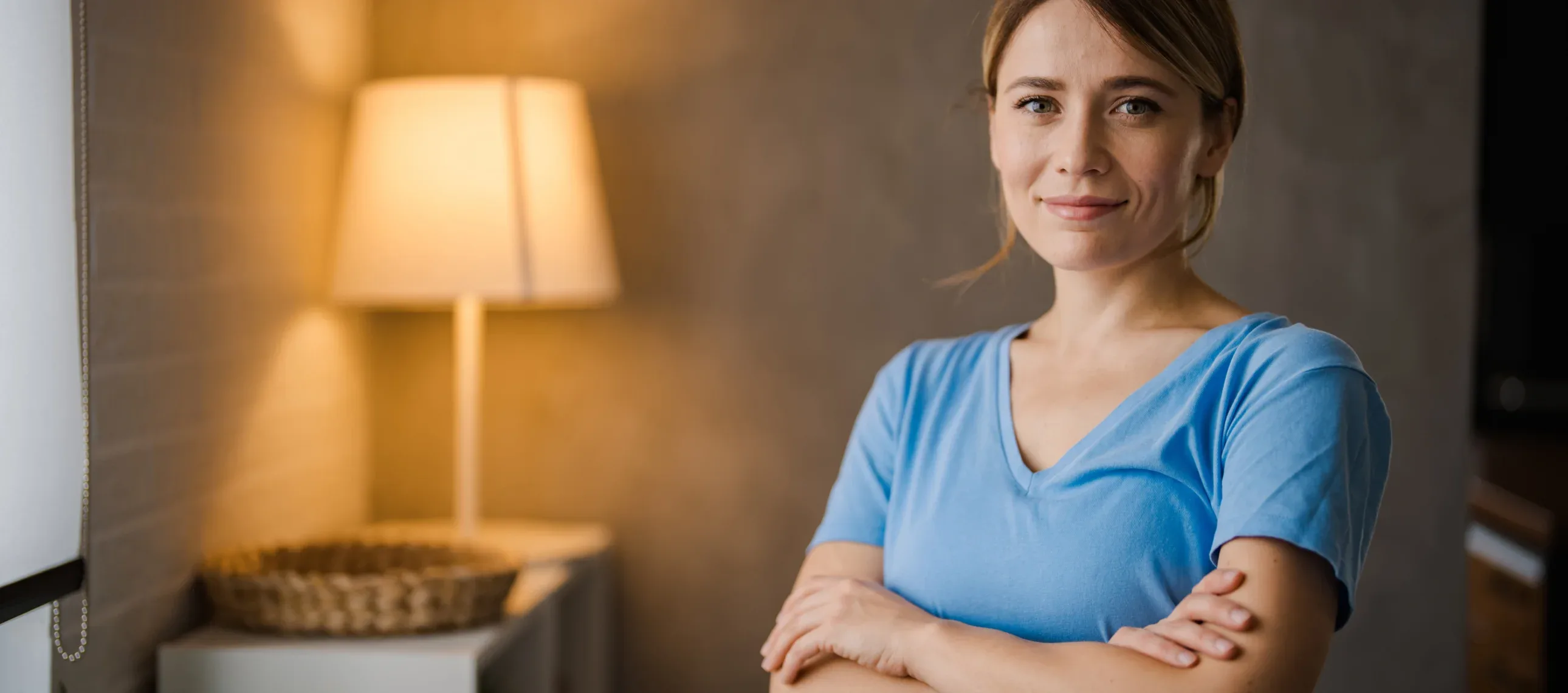 A woman wearing a blue shirt stands confidently in front of a stylish lamp, creating a warm and inviting atmosphere.