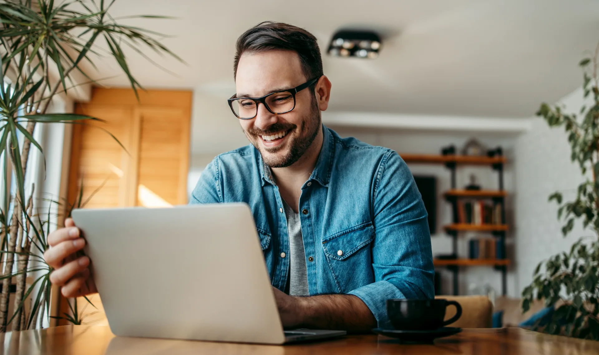  A cheerful man in glasses uses his laptop, embodying a blend of concentration and happiness in his work environment.