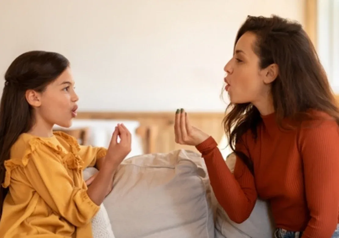 A woman and a little girl are seated on a couch, engaged in a delightful conversation, radiating warmth and happiness.