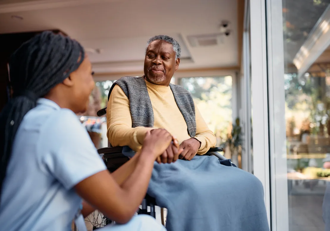 An elderly man in a wheelchair shares a moment of dialogue with a nurse, emphasizing the connection between patient and caregiver.