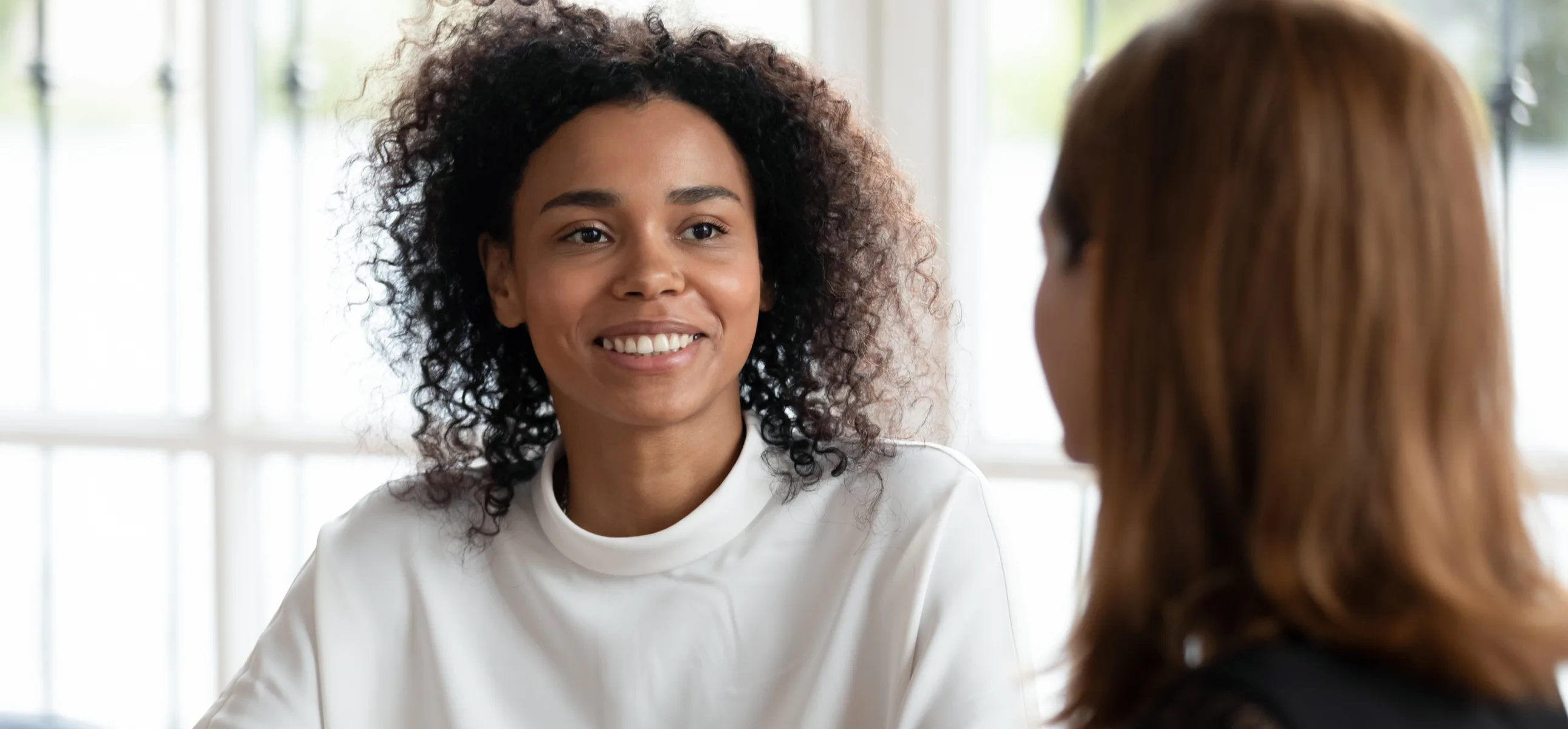 Two women are conversing, exchanging thoughts and smiles in a warm and inviting atmosphere.