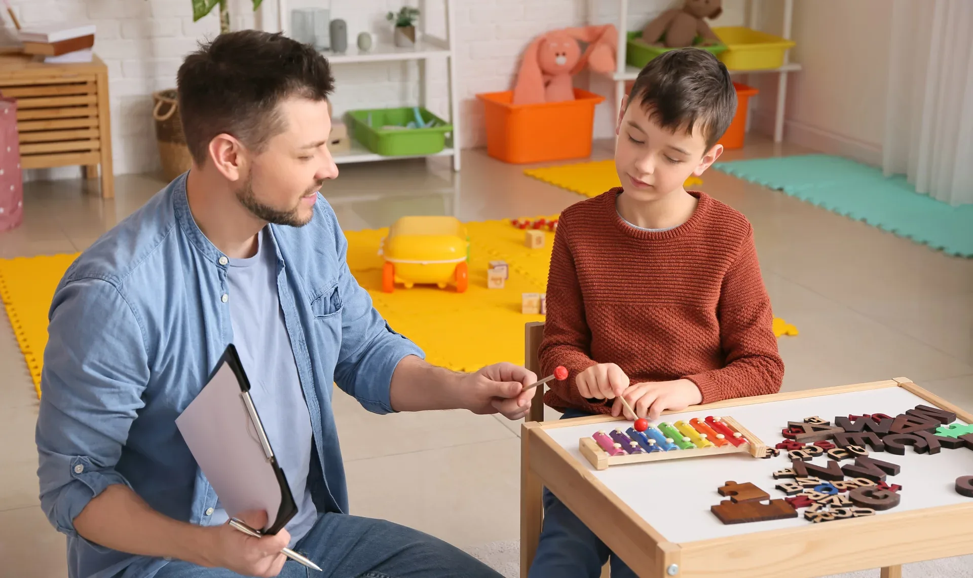 A man and a boy are seated at a table, reviewing notes on a clipboard together, engaged in a discussion.