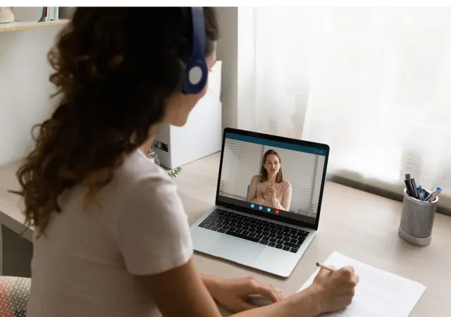 A woman sits at a desk with a laptop, engaged in a video call, focused and professional in her workspace.