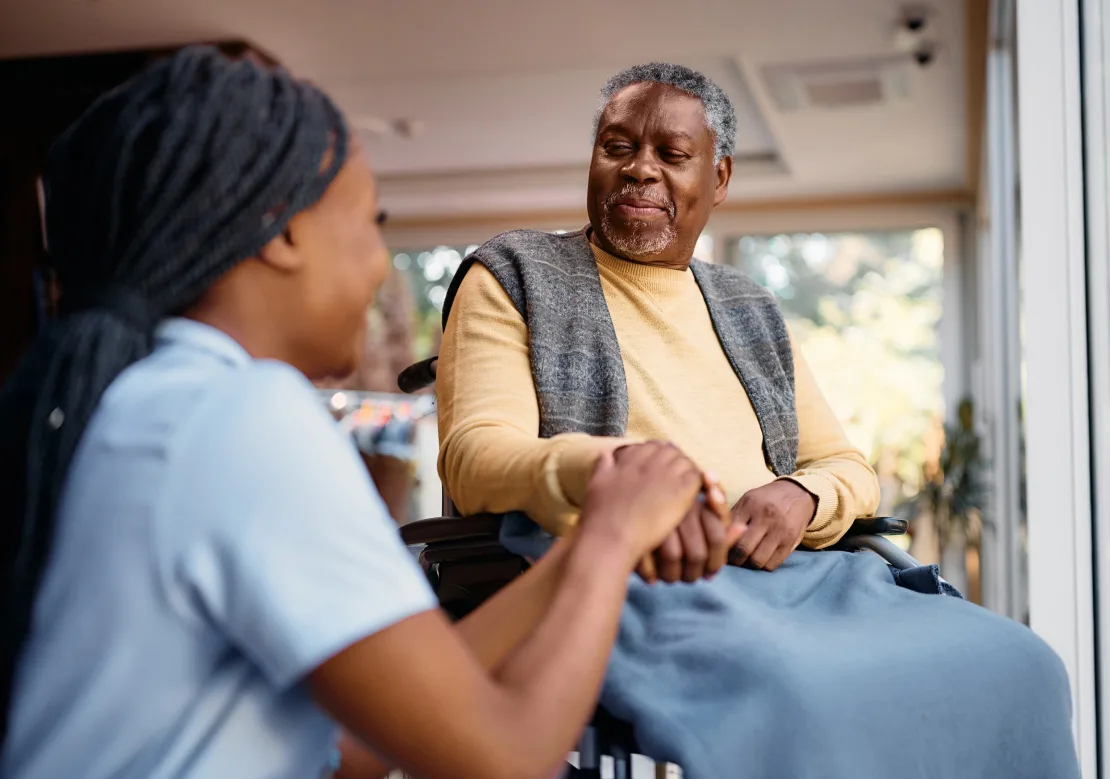 A woman in a wheelchair lovingly holds the hand of an elderly woman, illustrating a bond of friendship and empathy.